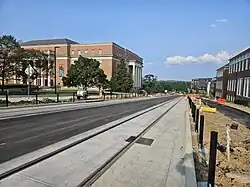 A pair of light rail tracks run along a road with two large buildings on either side.