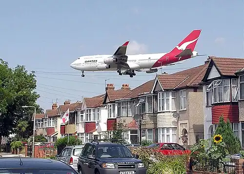 A landing Qantas Boeing 747-400 passes close to houses on the boundary of London Heathrow Airport, England.