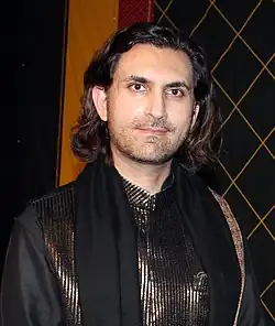 Rahul Sharma wearing a traditional South Asian outfit, standing in front of a dark background, looking directly at camera and smiling