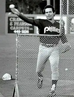 A man in light baseball pants and a dark jersey throwing a baseball during batting practice
