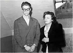 Black and white photograph of a handcuffed man with a woman at his side.