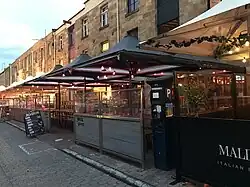 a brick facade building with some fairy lights and black and white gazebos over squared divisions.