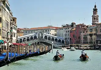 Gondoliers row past a row of gondolas on the Grand Canal near Rialto Bridge