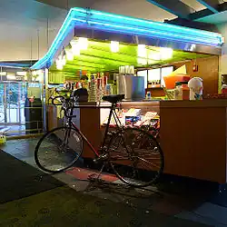 A bike sits parked before an indoor snack bar illuminated with blue neon lights.