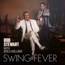 Stewart and Holland both seated and wearing suits, with Holland behind Stewart, and Stewart holding a glass of alcohol in his hand