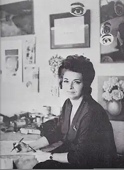 Rosa Rosenberg at her some studio in Mexico City, she is holding pens and brushes, and some of her artwork is visible in the background.