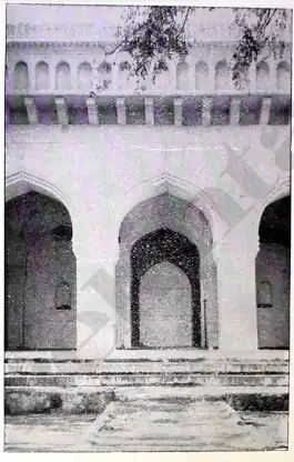 Black-and-white close-up of three arched entrances, with the central arch fully visible and two partially visible on either side. Above the arches, a parapet runs across the image.