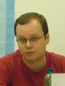 Saša Gedeon wearing glasses and red t-shirt, looking at camera