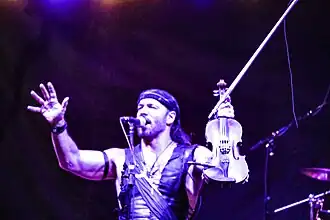 Scott Jeffers Traveler standing onstage, holding up a violin and singing into a microphone