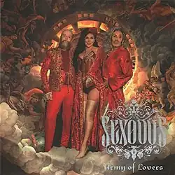 All 3 members of Army of Lovers clad in red, with gold accents. They are standing on clouds, in front of a fiery disc. They are surrounded by painted beings; likely angels. Dominika is sticking one of her legs out. The logo for the album and band is in the bottom right corner, coloured in periwinkle.