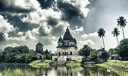 Image 1The pictured Shiva Temple is situated in Puthia Bazar of Rajshahi District. It was built on a hing plinth on the southern bank of a large tank. The temple is a 19.81 meter square building and total height is 35.03 meter. It is a Pancha Ratna type building consists of a Garbhagriha and a surrounding verandah. Rani Bhubanmoye Debi built this temple in 1823 AD. Photo Credit: Nasir Khan Saikat
