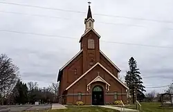 dark red brick church with a tall steeple. St. Edward's cemetery is visible in the far background