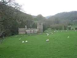 A church in a steep narrow valley, with a tower on the right (westwards), and the main church building being roofless