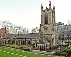 A substantial stone church seen from the north-west. The tower has crocketted pinnacles, and the north wall of the body of the church has a series of large rectangular windows