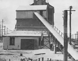 Covered conveyor leading upward and into the side of an industrial sheet metal building