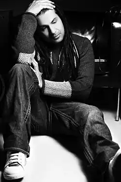 black-and-white image of Apache Indian wearing jeans and a sweater, sitting on the floor, with head propped up in right hand, looking right of camera
