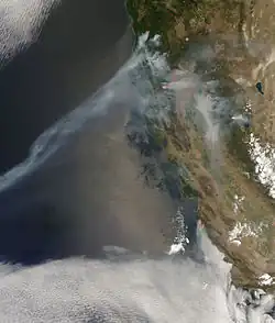 A satellite image showing a trail of smoke caused by several wildfires emanating from Northern California. The Pacific Ocean is visible to the left of the image.
