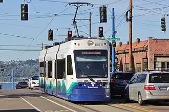 A short train traveling in the center of a street, passing several cars.