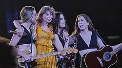 Taylor Swift performing in an orange dress with the Haim sisters