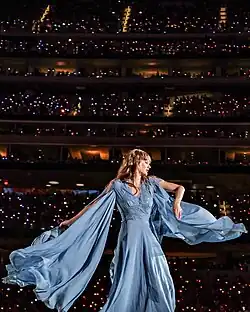 Swift dressed in a white gown, singing into a microphone.