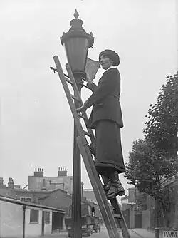 A lamplighter using an extension ladder to clean a street lamp