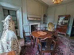 A sitting room with painted wood-panelled walls, and wooden furniture including a table and chairs, as well as a sideboard.