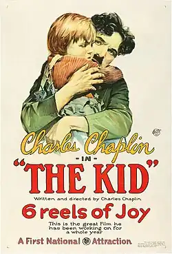 An illustration of the Tramp holding his titular Kid in front of a white background. Below the illustration states the author, film title and description: "Charles Chaplin -in- 'THE KID' – Written and directed by Charles Chaplin – 6 reels of Joy – This is the great film he has been working on for a whole year" The poster is underlined by a statement from its production company: "A First National Attraction".