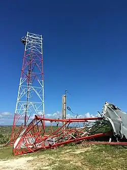A daytime image of a communication tower with its damaged top half on the ground