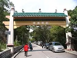 Cars parked on one-side of a tree-lined street with pedestrians walking under an archway which crosses the street