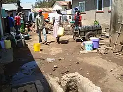 Men and women fill up water outside a shack dwelling