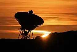 radio telescope dish silhouetted against a red sunset sky