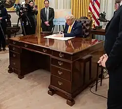 Donald Trump seated behind the C&O desk signing a large paper