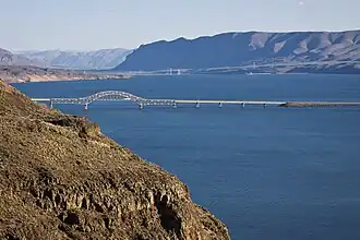 Photograph of a wide river framed by bare cliffs with a bridge in the distance.