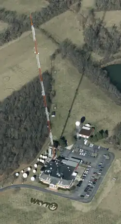 The WKYT facility, as seen from the air. It is set in a grassy field with a shaped hedge facing the road that spells out WKYT and a 27 in a circle. The studio building has a Colonial Revival-style facade. Also visible are a parking lot, satellite dishes, and two outbuildings.
