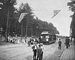 A crowd boarding a streetcar adjacent to a wooded park