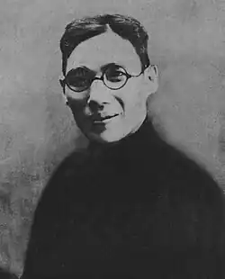 A black-and-white image of a smiling man wearing spectacles and a black shirt.